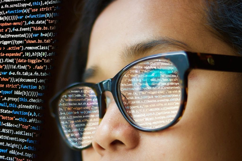 woman in glasses looking at screen full of computer code