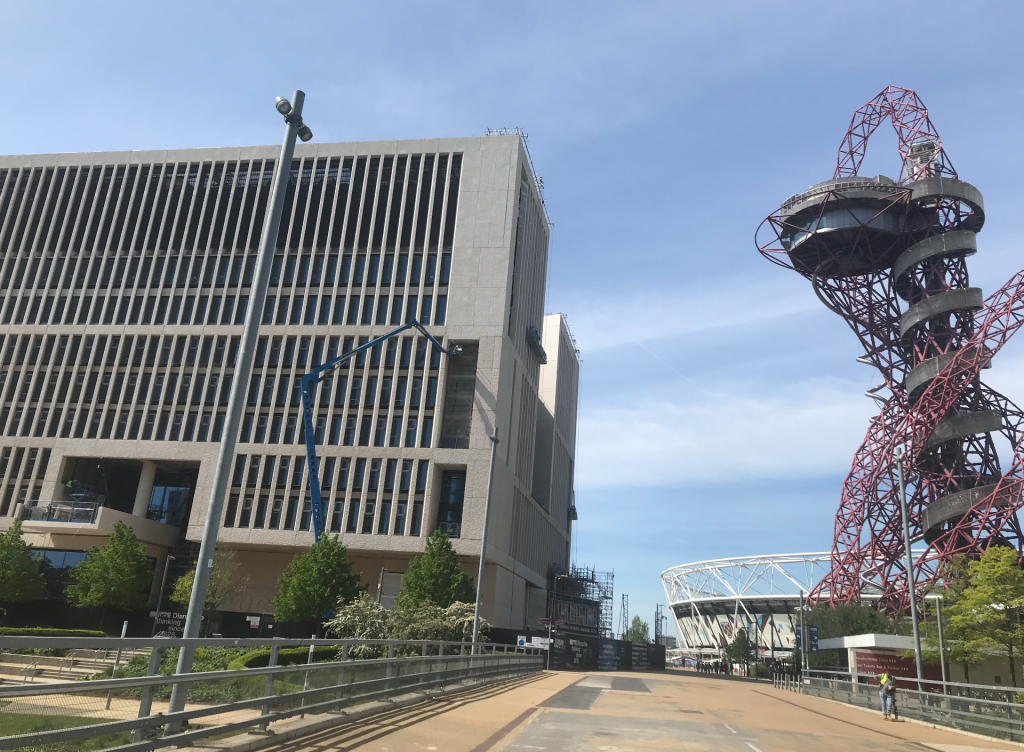the helter skelter building in stratford olympic park in london is a messy red scaffolding like structure and it sits on the right of this picture. The left is dominated by a huge concrete structure of eight floors with a wall of narrow windows that is the Marshgate building