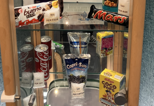 a display cabinet with items and the amount of sugar in them such as a coke can (27g), capri sun carton (24g) and mars bar (54g)